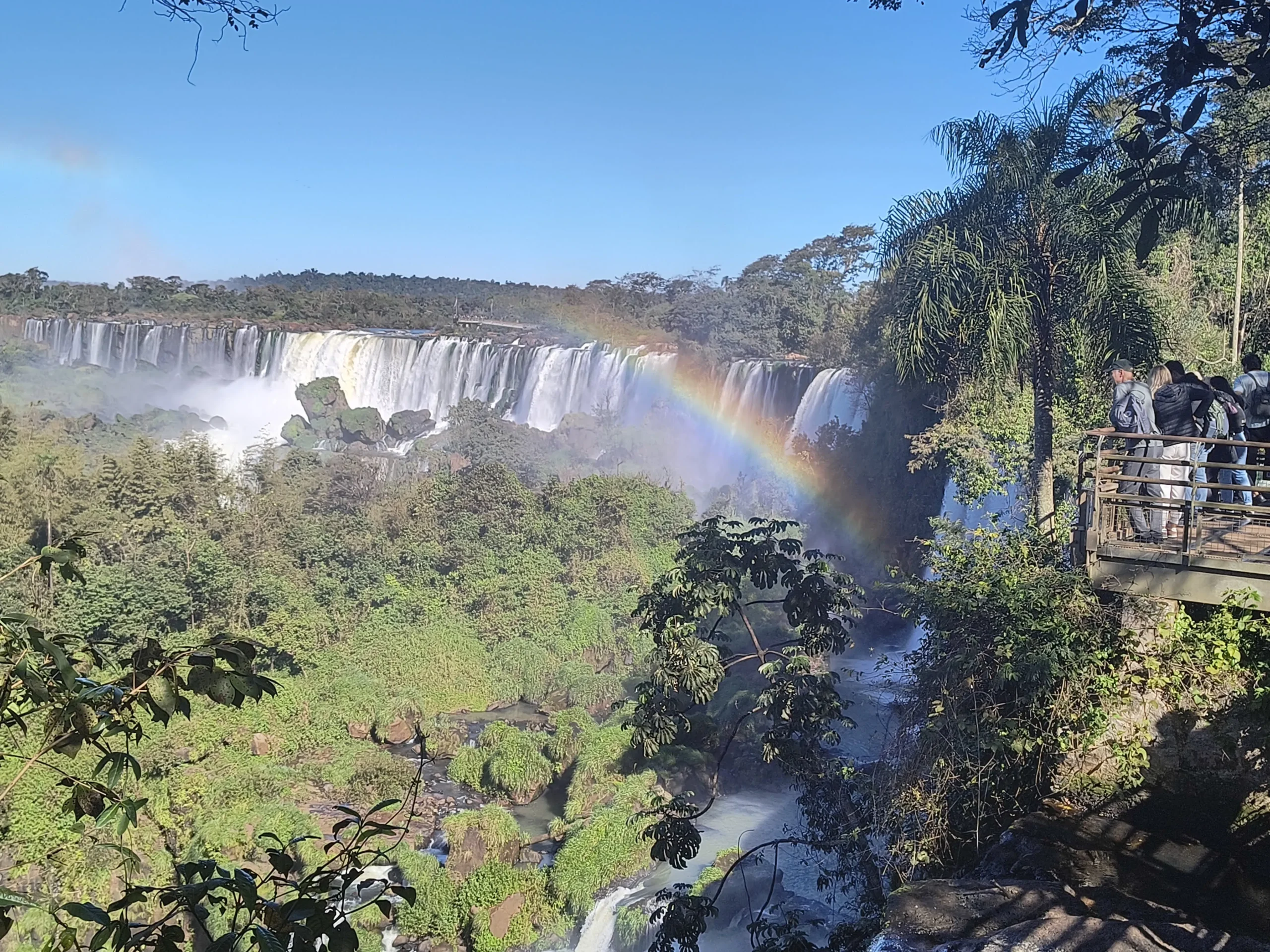 Iguazu Falls from the Argentine side, showing the extensive walkways and a beautiful rainbow over the powerful waterfalls, with tour guide Miguel.