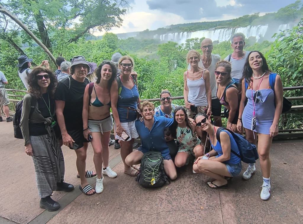 Group of happy tourists posing at a viewpoint overlooking Iguazu Falls, with tour guide Miguel, showcasing a memorable group travel experience.