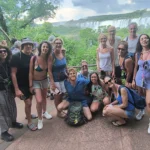 Group of happy tourists posing at a viewpoint overlooking Iguazu Falls, with tour guide Miguel, showcasing a memorable group travel experience.