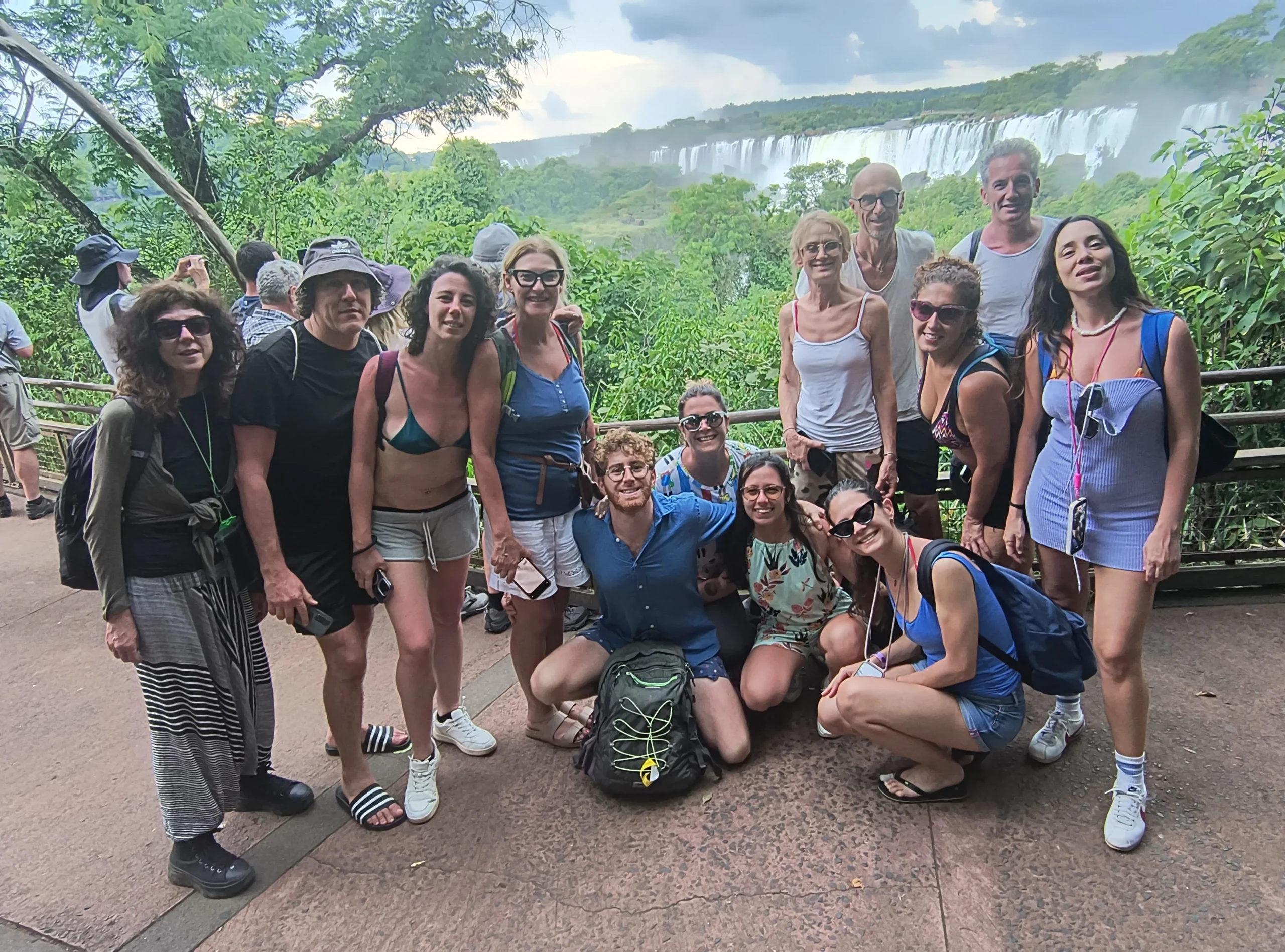 Group of happy tourists posing at a viewpoint overlooking Iguazu Falls, with tour guide Miguel, showcasing a memorable group travel experience.
